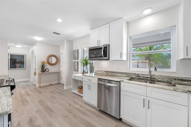 kitchen with appliances with stainless steel finishes, light stone countertops, light wood-style floors, white cabinetry, and a sink