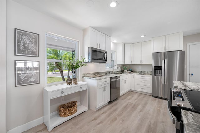 kitchen featuring light wood finished floors, stainless steel appliances, light stone counters, and white cabinets