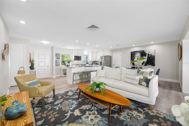 living room with baseboards, light wood finished floors, visible vents, and recessed lighting