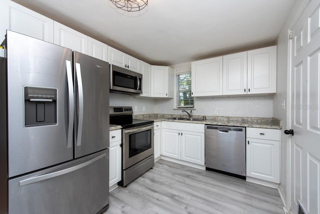 kitchen with sink, light stone countertops, light wood-type flooring, appliances with stainless steel finishes, and white cabinetry