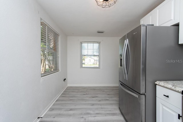 kitchen with light stone countertops, stainless steel fridge, light wood-type flooring, and white cabinetry