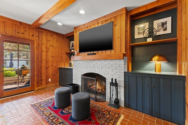 living room featuring wood walls, a fireplace, and beamed ceiling