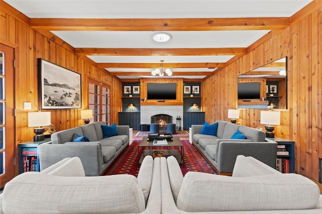 living room with wood walls, a chandelier, beam ceiling, and a brick fireplace