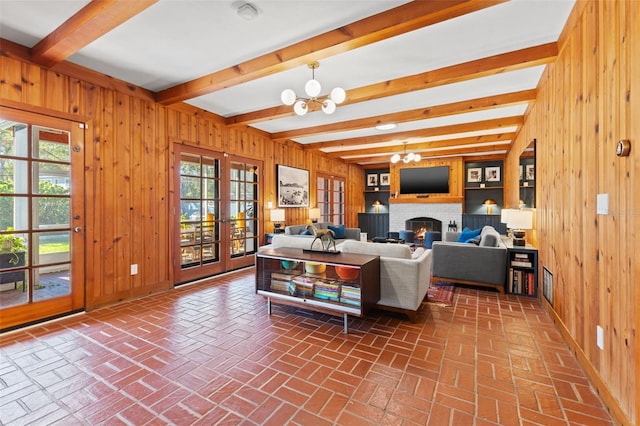 living room featuring wooden walls, french doors, beamed ceiling, and a notable chandelier