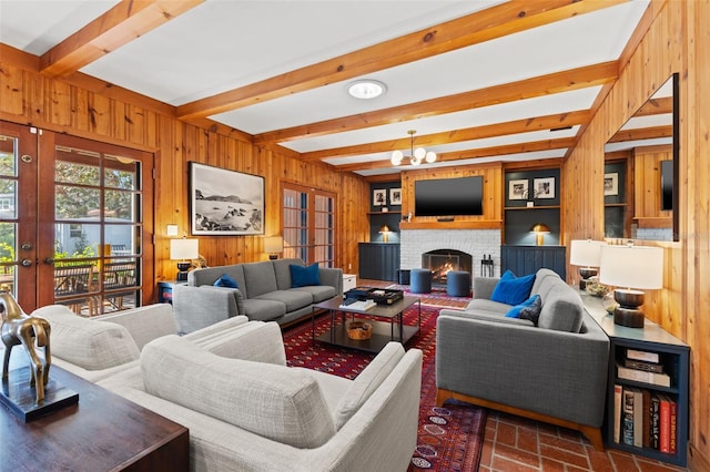 living room featuring french doors, a fireplace, wooden walls, an inviting chandelier, and beamed ceiling