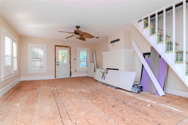 unfurnished living room featuring ceiling fan, baseboards, and stairs