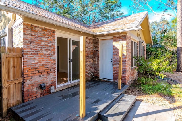 view of exterior entry with brick siding and a wooden deck