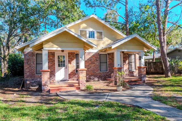 view of front of property with covered porch, brick siding, and fence