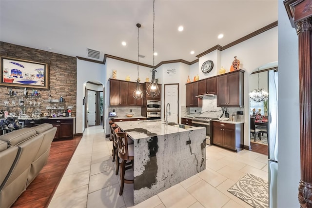 kitchen featuring light stone countertops, sink, hanging light fixtures, a center island with sink, and stainless steel stove