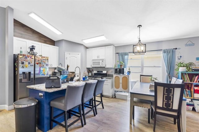 kitchen with stainless steel appliances, pendant lighting, white cabinetry, lofted ceiling, and an island with sink