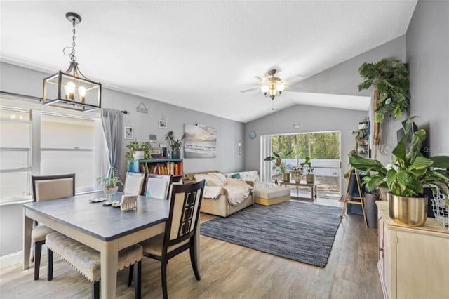 dining area featuring ceiling fan with notable chandelier, light wood-type flooring, and vaulted ceiling