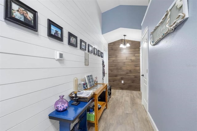 hallway featuring hardwood / wood-style flooring, a chandelier, wooden walls, and vaulted ceiling