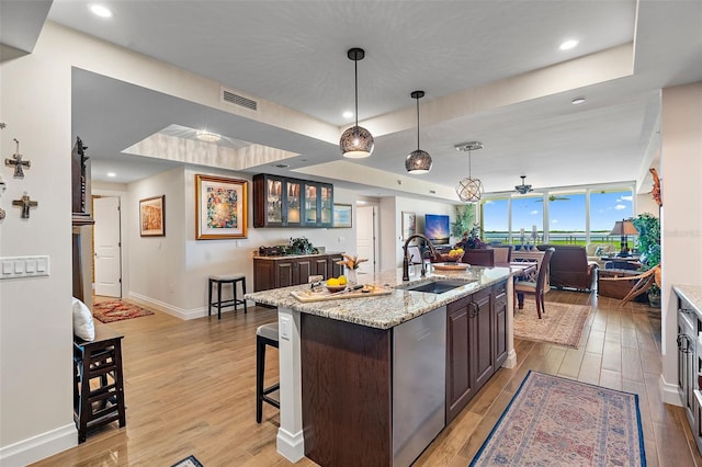 kitchen with stainless steel dishwasher, sink, hanging light fixtures, and light hardwood / wood-style flooring