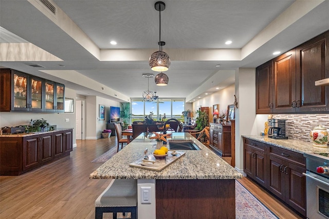 kitchen with sink, light hardwood / wood-style flooring, decorative light fixtures, a kitchen island with sink, and stainless steel stove