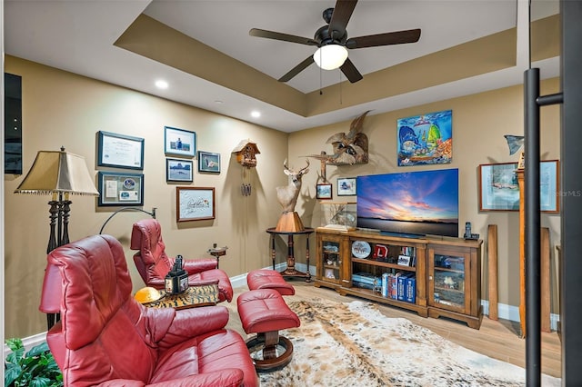 living room featuring ceiling fan, a tray ceiling, and light hardwood / wood-style flooring