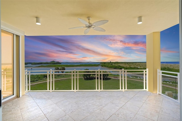 balcony at dusk featuring ceiling fan and a water view