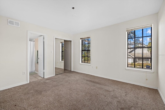 unfurnished bedroom featuring a closet, light colored carpet, visible vents, ensuite bathroom, and baseboards