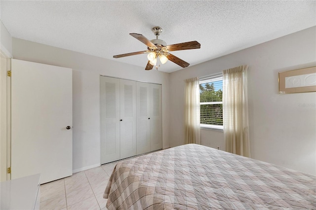 bedroom featuring ceiling fan, a closet, light tile patterned floors, and a textured ceiling