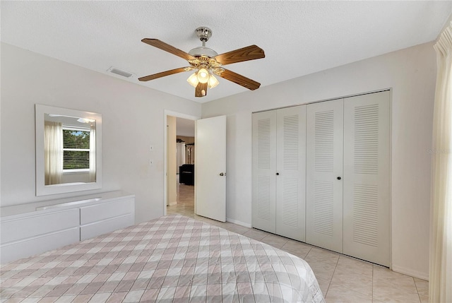 unfurnished bedroom featuring ceiling fan, light tile patterned floors, a textured ceiling, and a closet