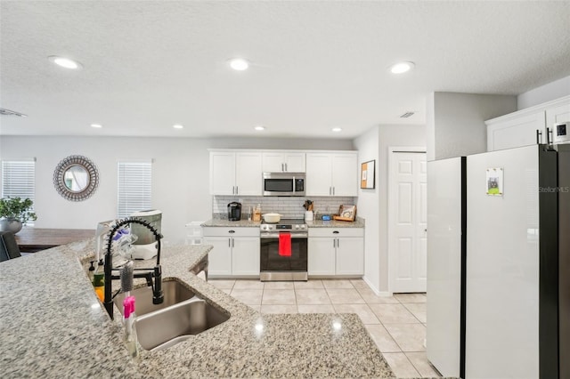 kitchen with white cabinets, stainless steel appliances, light stone countertops, and sink