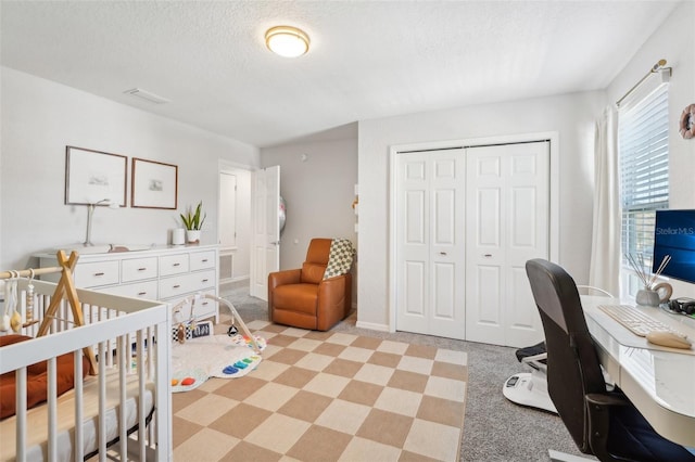 bedroom featuring a textured ceiling, a closet, light carpet, and a nursery area