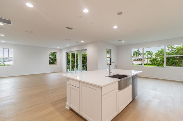 kitchen with white cabinets, sink, light hardwood / wood-style flooring, stainless steel dishwasher, and an island with sink