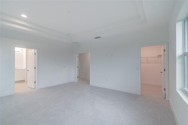 unfurnished bedroom featuring ensuite bathroom, a raised ceiling, a walk in closet, light colored carpet, and a closet