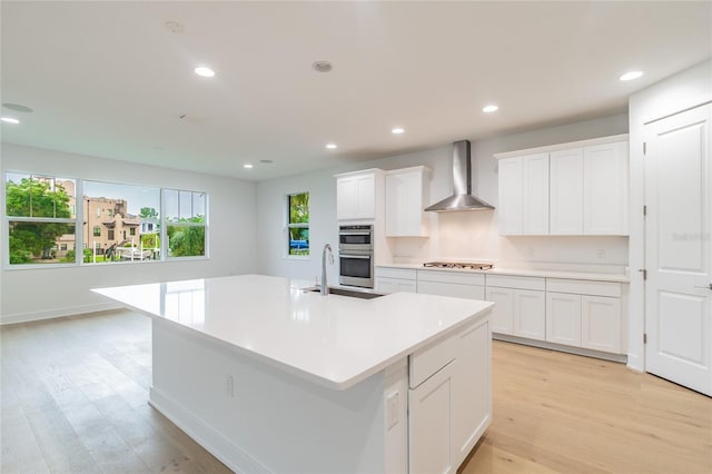 kitchen with wall chimney range hood, white cabinets, light wood finished floors, light countertops, and stainless steel appliances