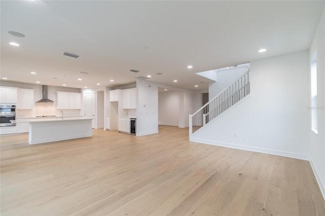 unfurnished living room with baseboards, visible vents, stairway, and light wood-type flooring