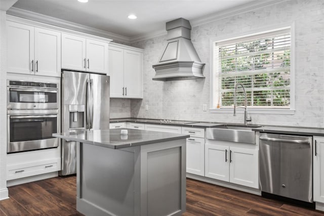 kitchen with appliances with stainless steel finishes, a kitchen island, custom exhaust hood, and white cabinets