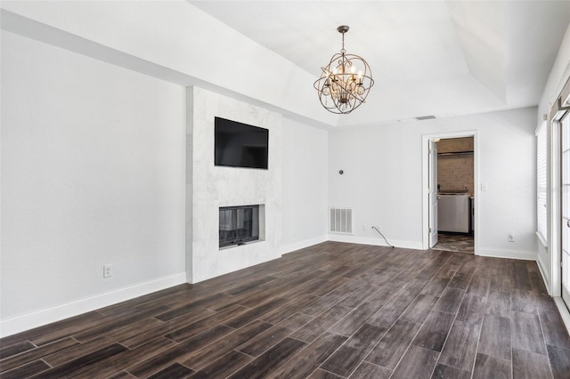 unfurnished living room featuring dark hardwood / wood-style flooring, a premium fireplace, a raised ceiling, and an inviting chandelier