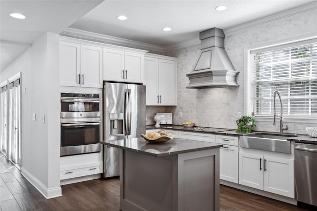 kitchen with sink, custom exhaust hood, appliances with stainless steel finishes, a kitchen island, and white cabinets