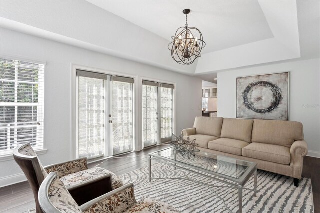 living room featuring an inviting chandelier, a healthy amount of sunlight, wood-type flooring, and a tray ceiling