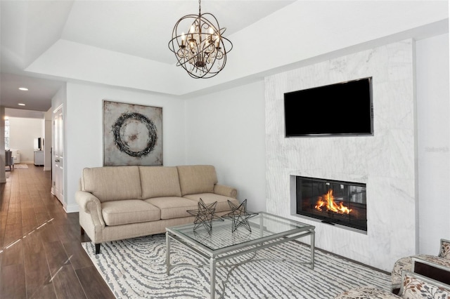 living room featuring a tray ceiling, hardwood / wood-style flooring, a premium fireplace, and a chandelier