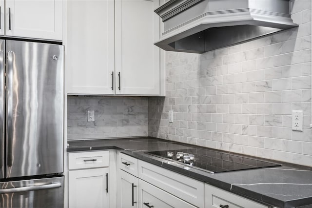 kitchen with black electric stovetop, stainless steel fridge, white cabinets, and premium range hood