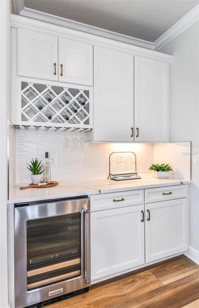 bar with crown molding, tasteful backsplash, light hardwood / wood-style floors, white cabinetry, and beverage cooler