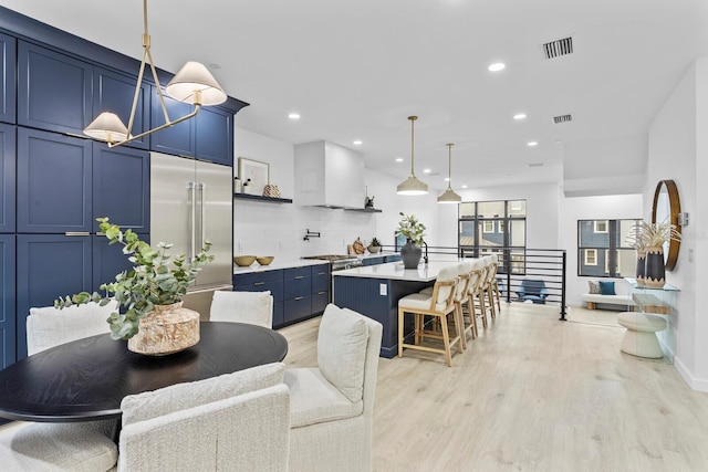 kitchen with built in fridge, blue cabinets, light hardwood / wood-style floors, decorative light fixtures, and a kitchen island