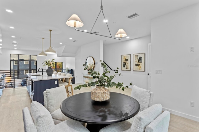 dining space with sink, light hardwood / wood-style floors, and a notable chandelier