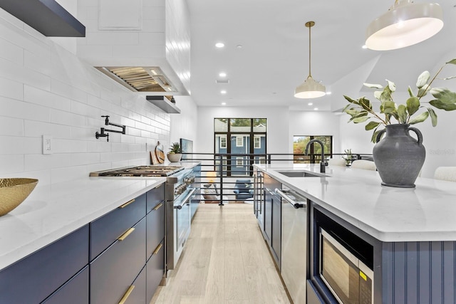 kitchen with light wood-type flooring, light stone counters, stainless steel appliances, sink, and decorative light fixtures