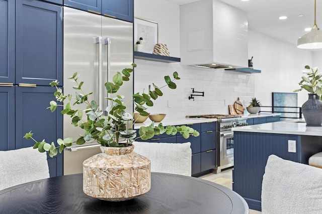 kitchen with premium range hood, tasteful backsplash, premium appliances, blue cabinets, and decorative light fixtures