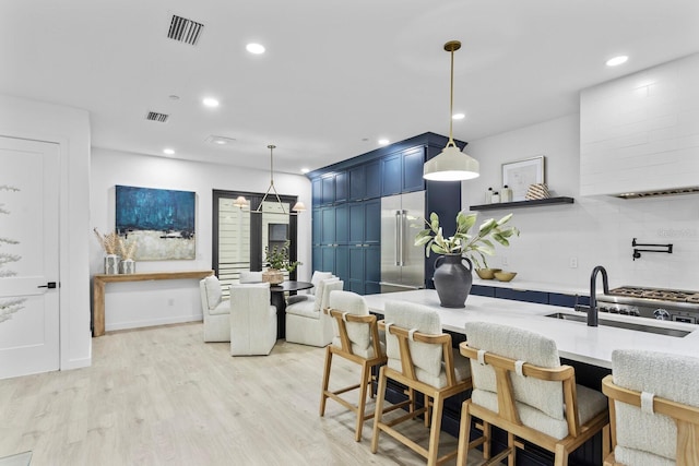 kitchen with light wood-type flooring, backsplash, sink, blue cabinetry, and decorative light fixtures