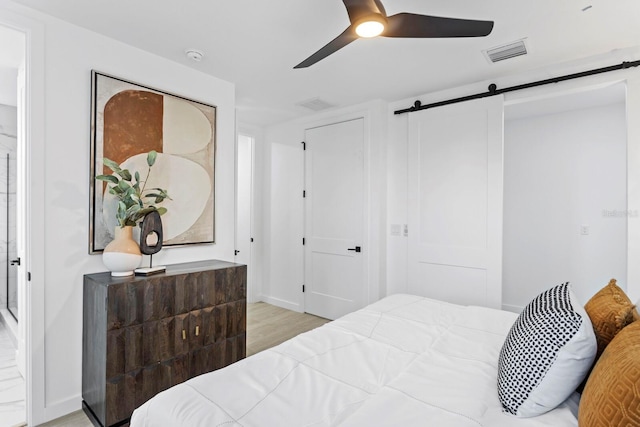 bedroom featuring ceiling fan, a barn door, and light hardwood / wood-style flooring