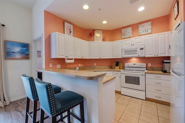 kitchen with kitchen peninsula, white cabinetry, and white appliances