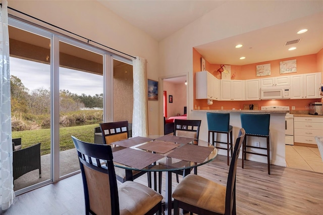 dining room with high vaulted ceiling, light hardwood / wood-style flooring, and plenty of natural light