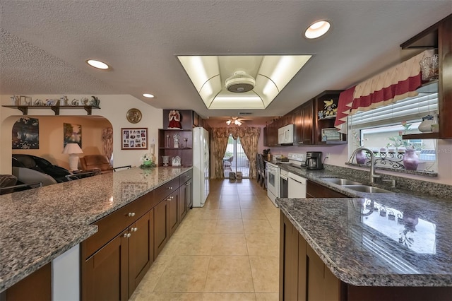 kitchen with a textured ceiling, white appliances, sink, dark stone countertops, and light tile patterned flooring