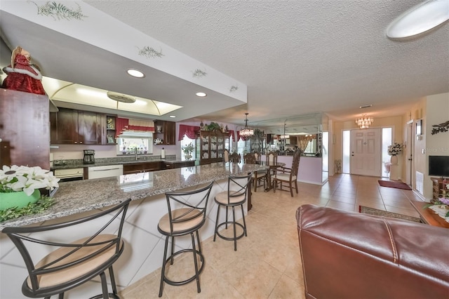 kitchen featuring pendant lighting, white dishwasher, a notable chandelier, a kitchen bar, and dark brown cabinetry