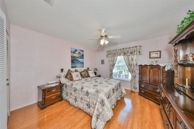 bedroom with a textured ceiling, light wood-type flooring, a closet, and ceiling fan