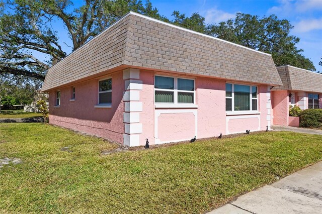 view of side of property with stucco siding, a shingled roof, mansard roof, and a yard