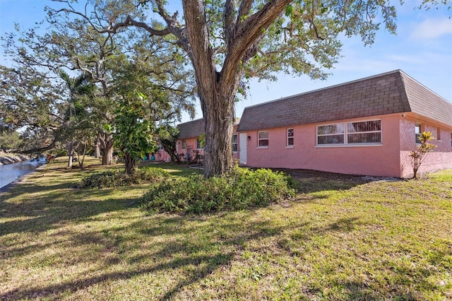 view of home's exterior with mansard roof, a lawn, a shingled roof, and stucco siding