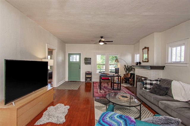 living room featuring ceiling fan, dark hardwood / wood-style flooring, a textured ceiling, and a brick fireplace